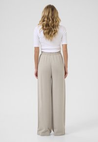 Light beige wide-leg trousers with a shimmery texture, featuring an elastic waistband and a loose fit, paired with a white cropped top.