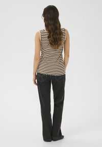 Stripet ribbet tanktop i brun og creme, med bølgede kanter. Båret sammen med sorte flared jeans og flade sko.