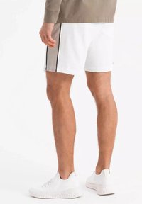 Shorts blancs avec des rayures latérales noires, en coton, avec une taille élastique, comprenant une poche arrière ; associés à des baskets blanches.