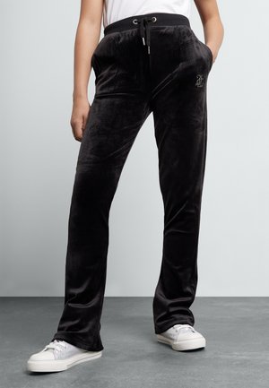 Pantaloni sudati in velluto nero con vita elastica, dettaglio con cordoncino, tasche laterali e un piccolo accento decorativo sulla tasca.