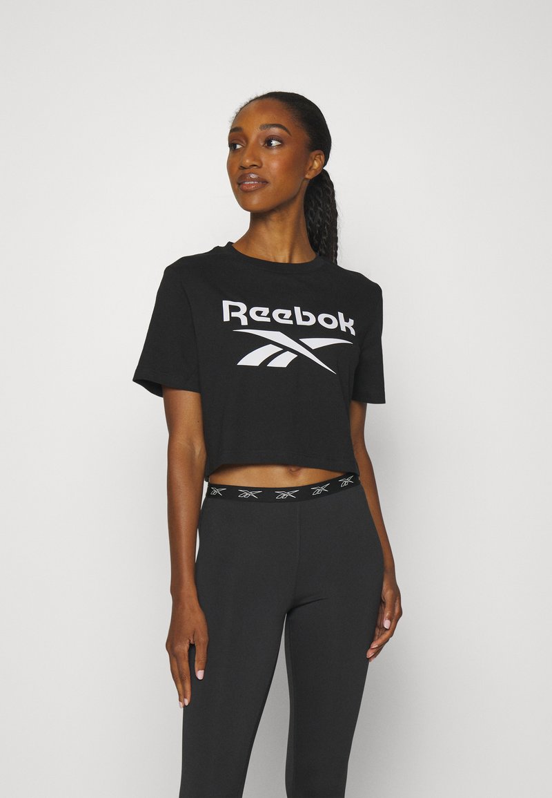 Čierne skrátené tričko s veľkým bielym logom Reebok, v kombinácii s čistými čiernymi legínami s pásom s nádychom a značkovaním Reebok.