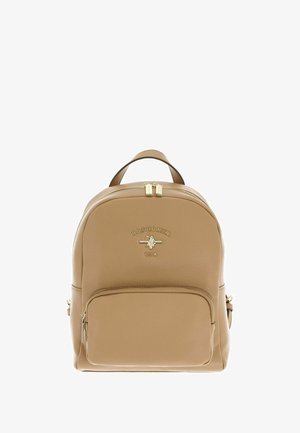 Mochila de polipiel color canela con forma redondeada, herrajes dorados, bolsillo frontal con cremallera y logo en relieve. Asa doble superior y correas ajustables.