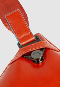 Borsa in pelle rossa con finitura lucida, caratterizzata da una tracolla con accenti blu e chiusura in metallo.