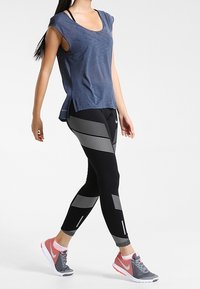 Námořnická modrá krátká halenka s volným střihem v kombinaci s černými legínami s bílými diagonálními pruhy a elegantními černými teniskami s růžovými akcenty.