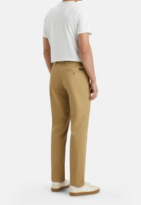 Chinos beige à coupe droite, poche arrière boutonnée et t-shirt blanc décontracté. Des baskets blanches avec des semelles beiges sont portées.