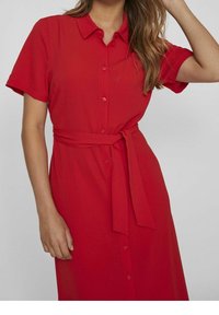 Robe chemise rouge à manches courtes, avec patte de boutonnage à l'avant et ceinture en tissu. Confectionnée dans un matériau léger à la texture lisse.