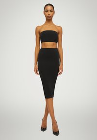 Ensemble noir deux pièces comprenant un crop top sans bretelles et une jupe midi ajustée. Texture lisse avec un design minimaliste et une coupe à mi-genoux.