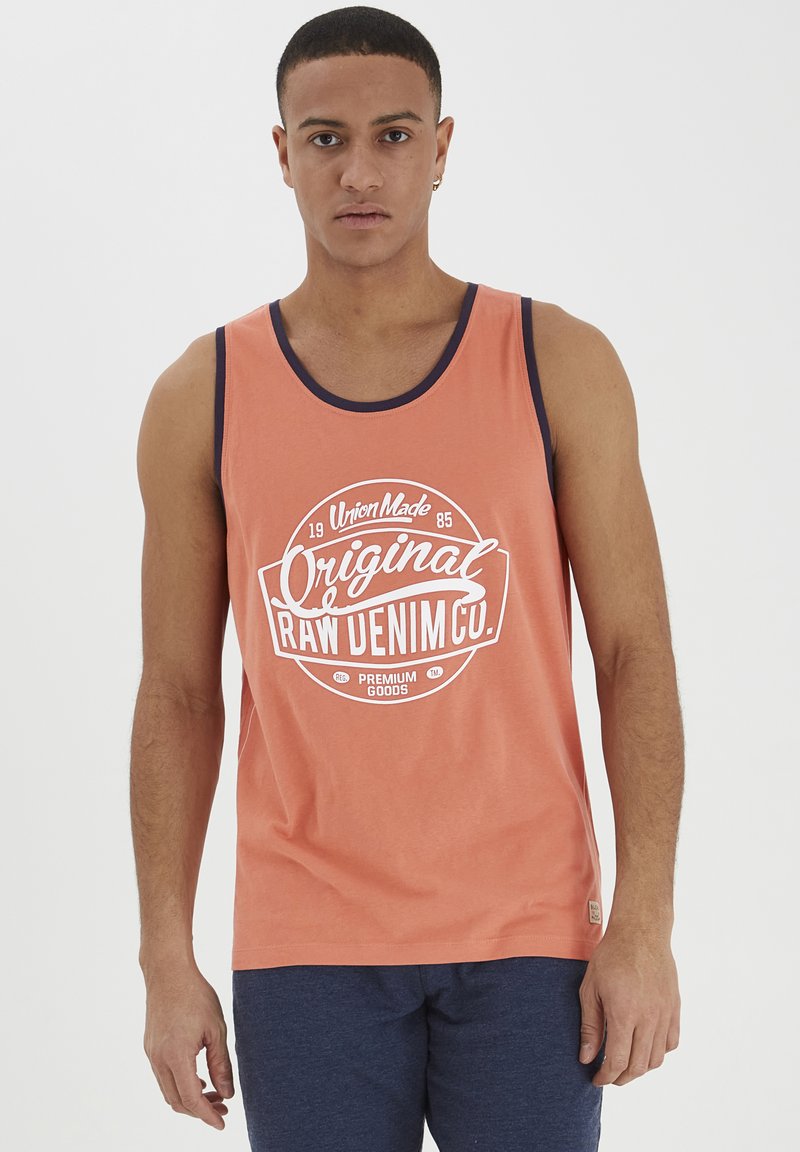 Top sin mangas naranja con escote navy, con un estampado gráfico blanco que dice "Original Raw Denim Co." Material de algodón ligero.