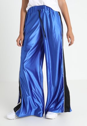 Blue satin wide-leg trousers with side slits, black side panels, adjustable waistband, and drawstring detail. Paired with white shoes.