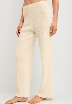 Beige textured wide-leg pants worn bare feet, with relaxed fit and elastic waistband, shown from waist to feet on neutral background.
