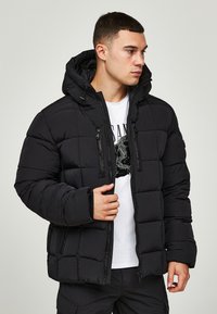 Schwarze Steppjacke mit einem gesteppten Design, vorderem Reißverschluss, verstellbare Kapuze und zwei Reißverschlusstaschen. Weiches, leichtes Material.