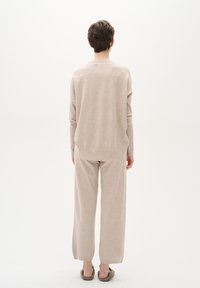 Un maglione lavorato a maglia beige presenta una vestibilità morbida con maniche lunghe. Abbinato a pantaloni larghi coordinati per un look armonioso. Texture morbida.
