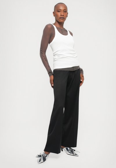 White tank top, sheer brown long-sleeve shirt, black wide trousers, and shiny silver high-heeled shoes with a bow detail.