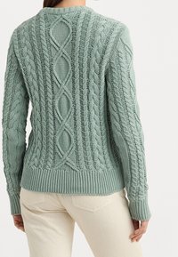 Ljusgrön stickad tröja med ett texturerat kabelmönster, ribbade ärmslut och nederkant, samt en dekorativ detalj på baksidan i form av en diamant.