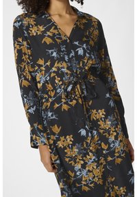 Czarna sukienka z długimi rękawami, w kwiatowy wzór w złotych i niebieskich odcieniach. Ma zapięcie na guziki z przodu oraz elastyczny pasek w talii, co umożliwia regulację dopasowania.