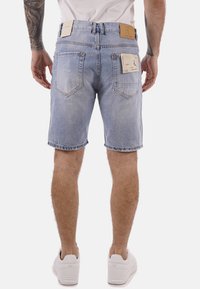 Shorts di denim blu chiaro con una finitura sbiadita. Presentano tasche, etichette sul retro e un orlo dritto. Indossati con sneakers bianche.