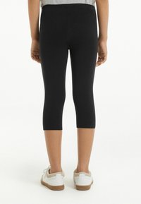 Leggings capri noirs en matériau extensible, avec une taille haute et une texture lisse. Associés à des baskets blanches avec des accents beige.