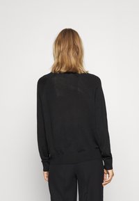 Svart stickad tröja med avslappnad passform, långa ärmar och ribbad nederkant. Tyget verkar mjukt, med en något genomskinlig textur.