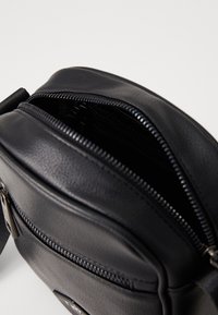 Black leather crossbody bag with a top zipper. Features multiple compartments and smooth texture, designed for casual use.