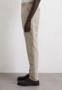 Light beige chinos with an elastic waistband, side pockets, and a slim fit, paired with black slip-on shoes. Smooth fabric texture.