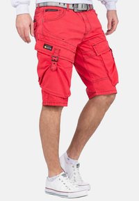 Rode cargoshorts van katoen met meerdere zakken, verstelbare straps en een ontspannen pasvorm. Gepaard met witte sneakers.
