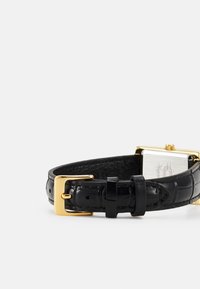 Black leather watch strap with a textured crocodile skin pattern, featuring a gold metal buckle and rectangular silver watch face.