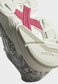 Adidas-sneaker med vit sula och övre del i texturerad grå tyg. Har rosa Torsion-accent och mönstrad greppdesign på undersidan.