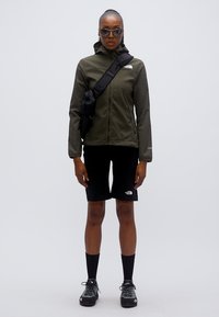 Πράσινο μπουφάν ελιάς, μαύρο σορτς, μαύρες κάλτσες και γκρι παπούτσια. Το μπουφάν είναι εφαρμοστό, με φερμουάρ στο μπροστινό μέρος και λεπτομέρεια λογότυπου. Το σορτς έχει λογότυπο στο πόδι.