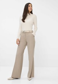 Pantalons longs beiges à coupe droite, en tissu texturé, avec une taille élastiquée et passants de ceinture. Associés à un haut crème à manches longues à côtes et des ballerines beiges.
