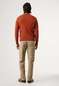 Suéter rojo de cuello redondo hecho de una tela suave, combinado con pantalones de sarga en un tono beige claro. Calzado casual completa el atuendo.