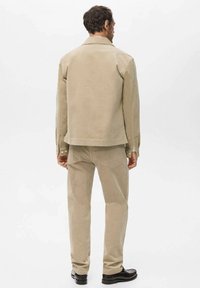 Beige corduroy jacket and pants set. The jacket features a collared neckline and buttons; the fabric has a textured finish. Black shoes complete the look.