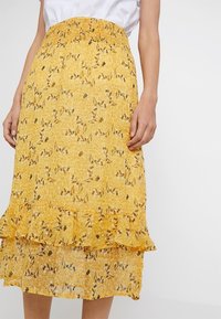 Gonna midi gialla a fiori con una vita elastica arricciata, orlo a volant a strati e delicati motivi neri di fiori in tutto il capo.