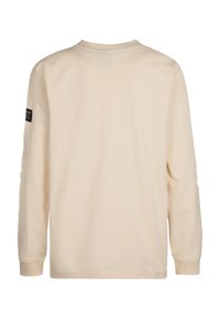 Tricou cu mânecă lungă de culoare bej deschis, cu guler rotund, având un etichetă neagră cusută pe mâneca stângă și o textură netedă din bumbac.