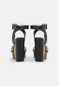 Svarta klacksandaler med en strukturerad ovandel, öppen baksida och spänne. Har kraftiga blockklackar och en mjuk innersula.