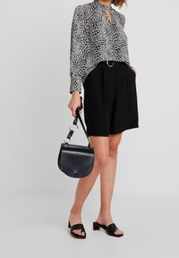Blouse à imprimé léopard noir et blanc avec un décolleté en forme de trou de serrure, associée à un short taille haute noir et un petit sac en cuir noir porté en bandoulière.