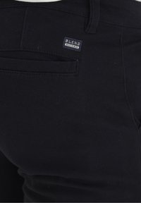 Pantalon en denim noir à la texture lisse, avec une poche arrière et une petite étiquette tissée portant l'inscription "BLEND" en bleu et blanc.