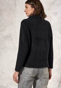 Svart, fluffig tröja med hög krage och långa ärmar. Baksidan har en slät yta och avslappnad passform. Kombineras med ljusgrå jeans.