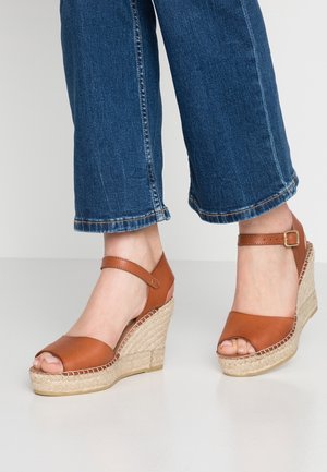 Brązowe skórzane sandały na koturnie z odkrytym palcem, wyposażone w obcas owinięty jutą, regulowany pasek na kostce oraz gładkie wykończenie.