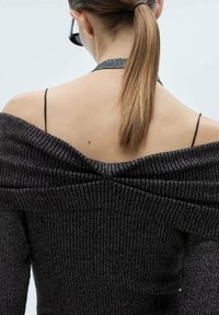 Svart off-shoulder tröja med texturerad stickad design och metalltrådinslag. Har tunna axelremmar och rynkor på baksidan.