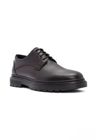 Chaussure en cuir noir avec un bout arrondi, un laçage et une semelle en caoutchouc épaisse dotée de rainures de traction pour une meilleure adhérence. Texture lisse avec des accents minimaux.