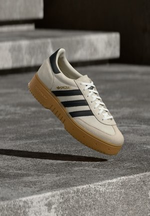 Beige suede sneaker with black stripes, white laces, and a gum rubber sole. Features "SPEZIAL" branding on the side.