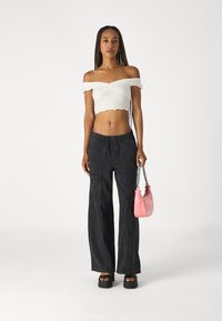 Hvit avkuttet off-shoulder topp med volanger, kombinert med løse svarte bukser med sidelommer. Holder en liten rosa håndveske.