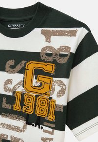 Zielona i biała koszulka w paski wykonana z organicznej bawełny. Posiada duży, żółty i brązowy grafikę z napisem "G 1981 L.A." oraz teksturowane nadruki.
