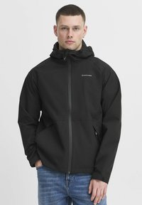 Črna vodoodporna jakna s kapuco, sprednjim zadrgo in logotipom. Ima sproščen kroj, elastične manšete in dva stranska žepa. Obuta preko modrih kavbojk.