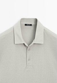 Polo shirt grigio chiaro realizzato in tessuto testurizzato, con colletto, tre bottoni e un'etichetta del marchio sul collo.