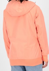 Peachfarvet jakke med hætte, fremstillet i et glat, letvægtsstof med ribbet manchetter og kant. Bagview viser en sømløs design.