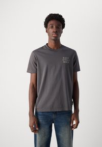 Grijze ronde hals t-shirt van zachte katoen, met een klein wit "MARC O'POLO DENIM" logo op de linkerborst, gecombineerd met vervaagde blauwe jeans.