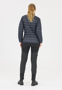 Geplüschte dunkelgraue Jacke mit horizontaler Naht, kombiniert mit schwarzen Hosen aus strukturiertem Stoff und verstellbaren Manschetten, getragen mit schwarzen Stiefeln.