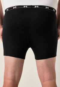 Černé bavlněné boxerky s elastickým pasem v bílé a černé barvě, na kterém je písmeno "M". Hladká textura, přiléhavý design.