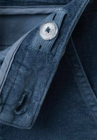 Tmavě modrá látka s jemnou texturou obsahuje viditelný detail knoflíku a smyčky. Design zahrnuje prošívání a oblast límce.